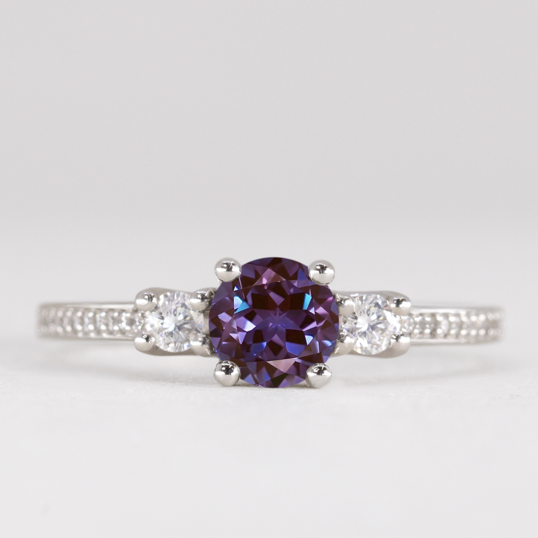 Round cut alexandrite and diamond trilogy engagement ring with white diamond pave band