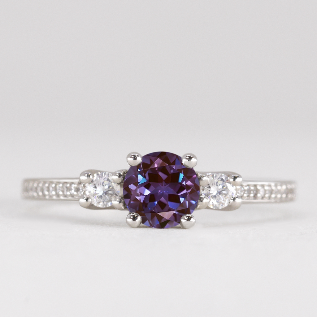 Round cut alexandrite and diamond trilogy engagement ring with white diamond pave band