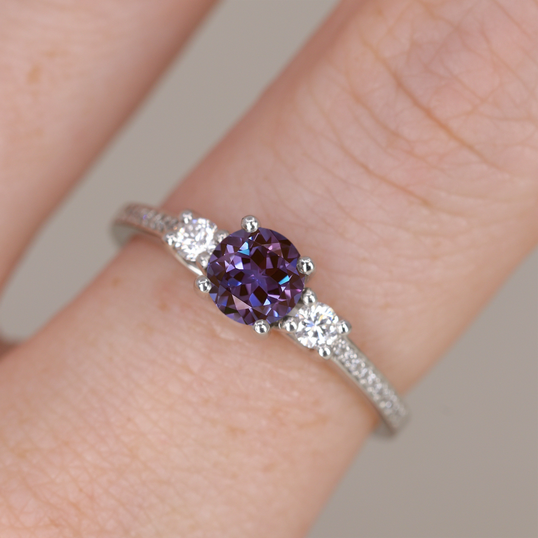 Round cut alexandrite and diamond trilogy engagement ring with white diamond pave band