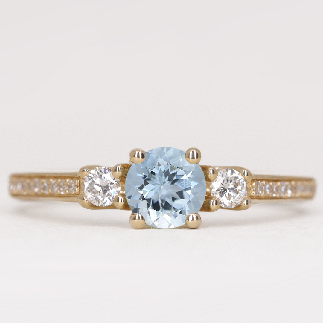 Round cut aquamarine and diamond trilogy engagement ring with white diamond pave band