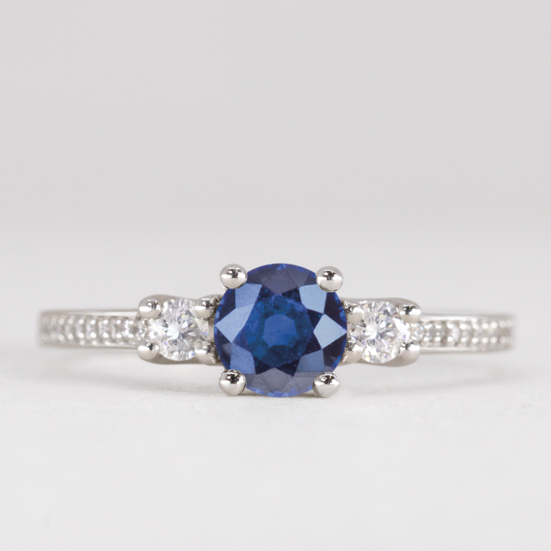 Round cut blue sapphire and diamond trilogy engagement ring with white diamond pave band