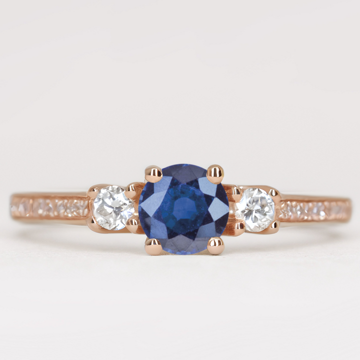 Round cut blue sapphire and diamond trilogy engagement ring with white diamond pave band