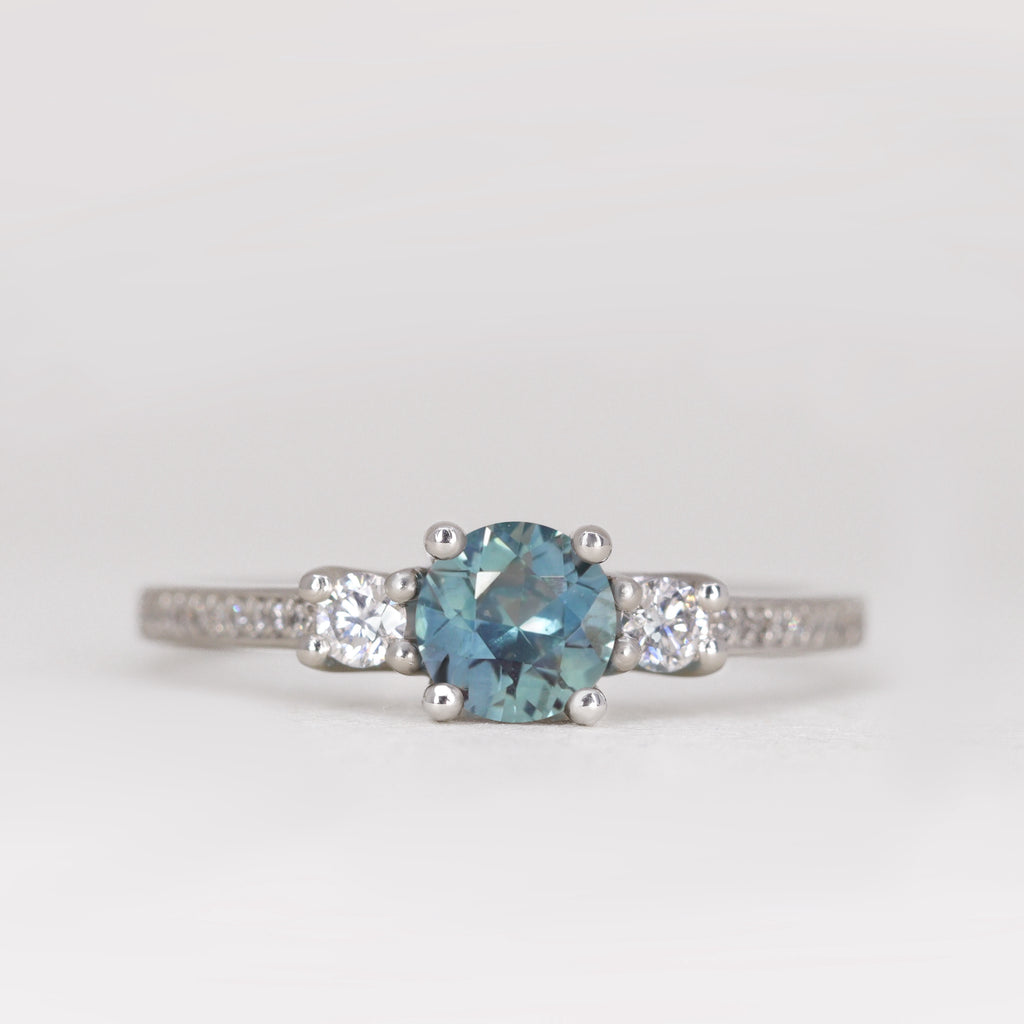 Round cut teal sapphire trilogy engagement ring with pave band