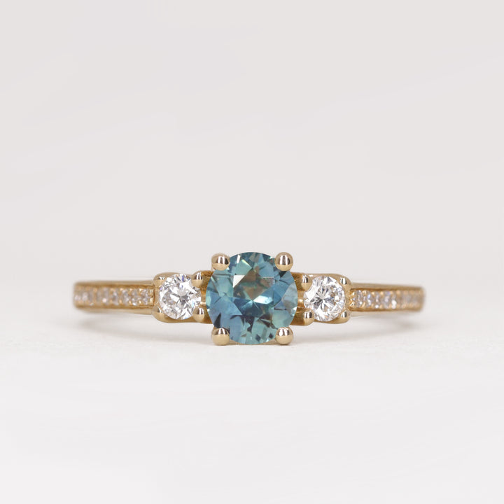 Round cut teal sapphire trilogy engagement ring with pave band