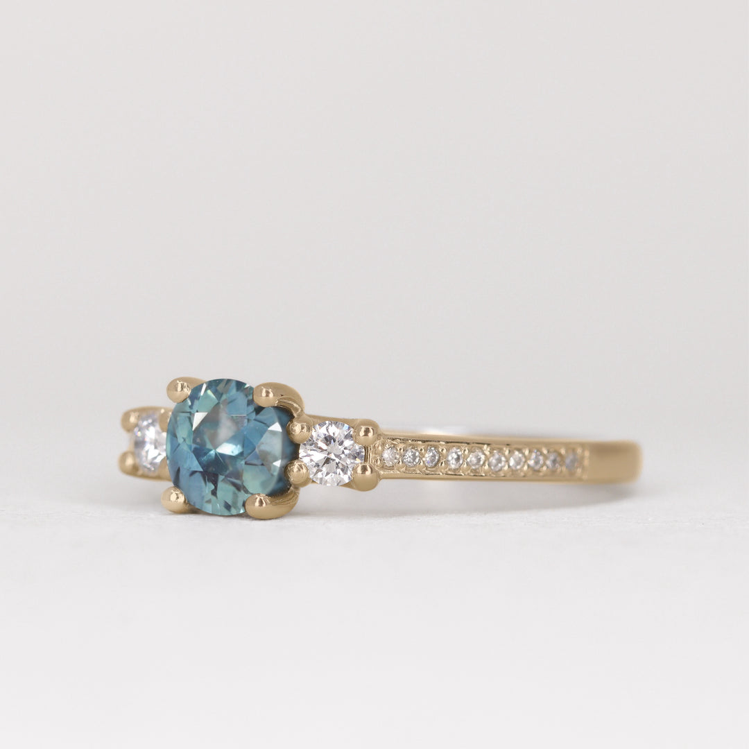 Round cut teal sapphire trilogy engagement ring with pave band