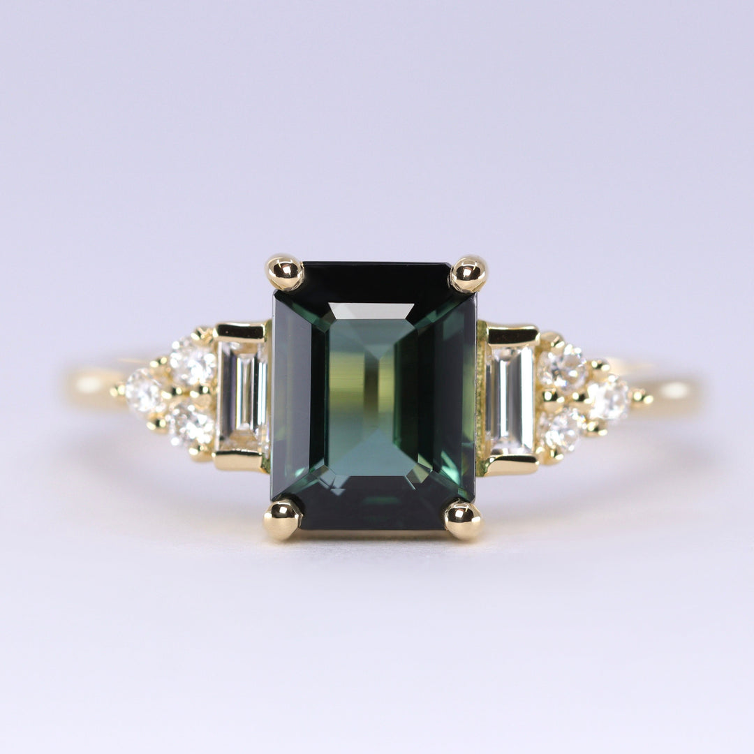 Gold ring with a green gemstone and smaller diamonds on a light gray background