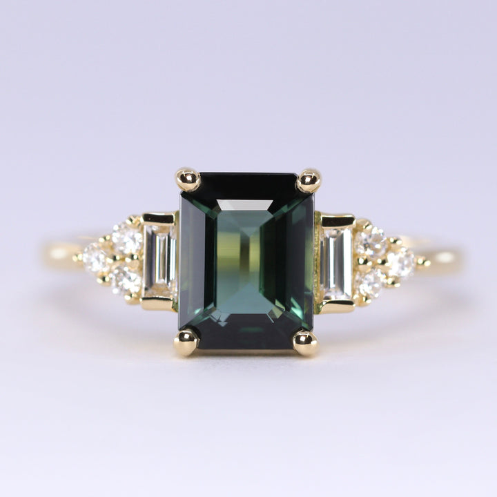 Gold ring with a green gemstone and smaller diamonds on a light gray background