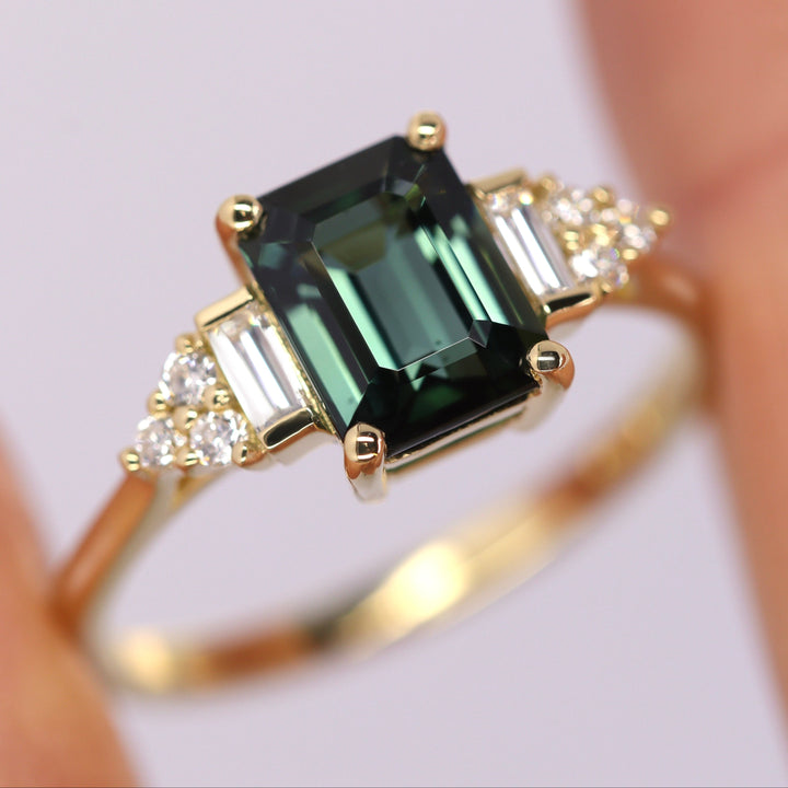 Gold ring with a green gemstone held by a hand on a white background