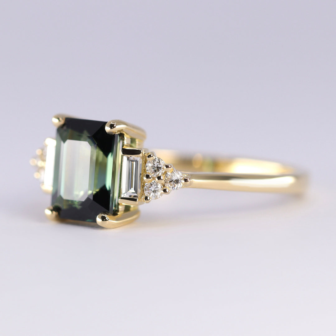 Gold ring with a green gemstone and smaller diamonds on a light gray background