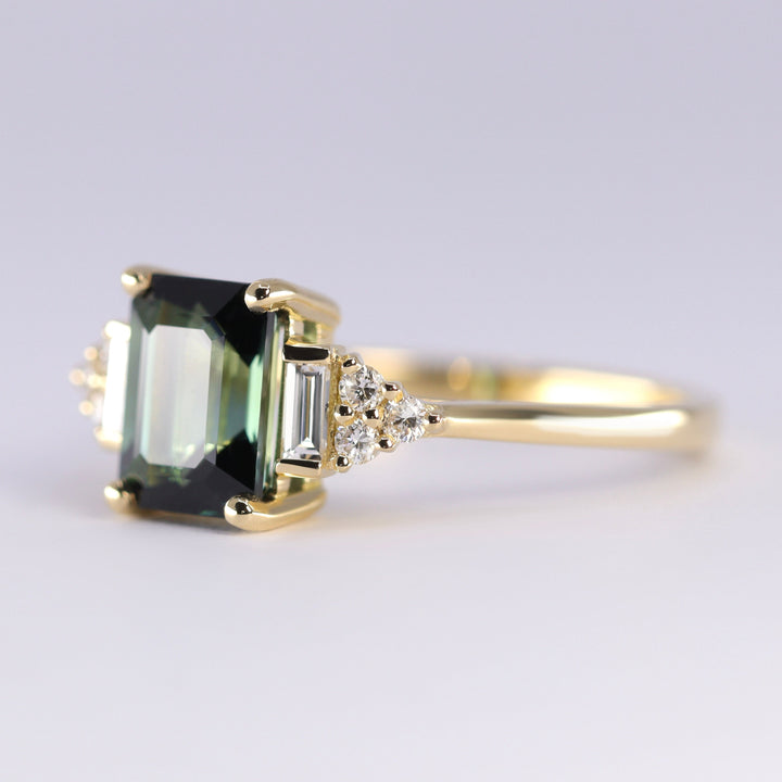 Gold ring with a green gemstone and smaller diamonds on a light gray background